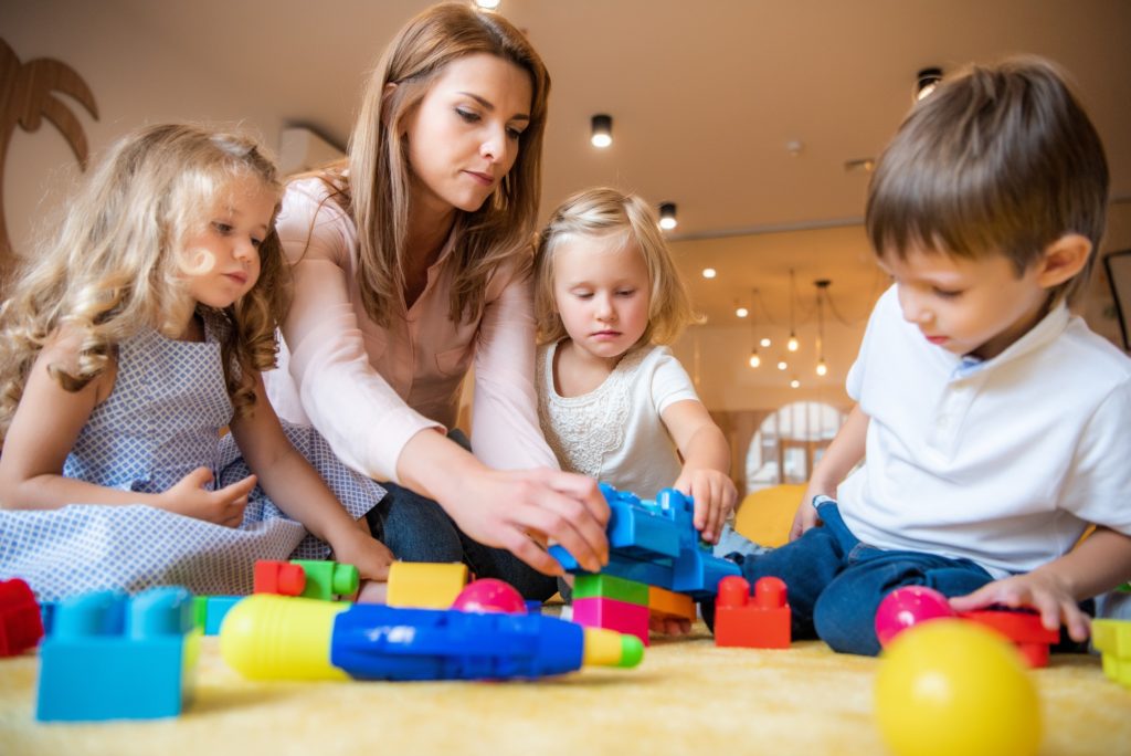 educator and adorable kids playing with constructor in kindergarten